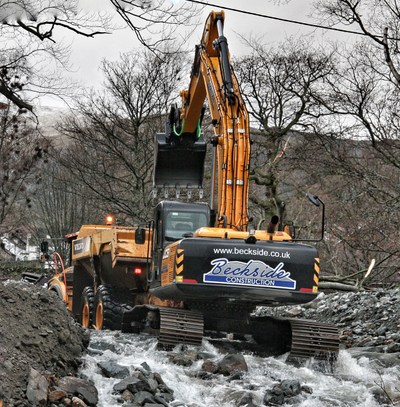 A Beckside construction excavator loading an SER dump truck in the river at Glenridding