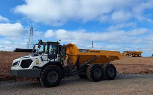 An SER Liebherr TA230 dump truck with distinctive white cab and a Volvo A30G dump truck parked under a blue sky