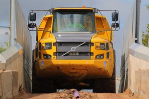 A large Volvo dump truck squeezing over a very narrow bridge.